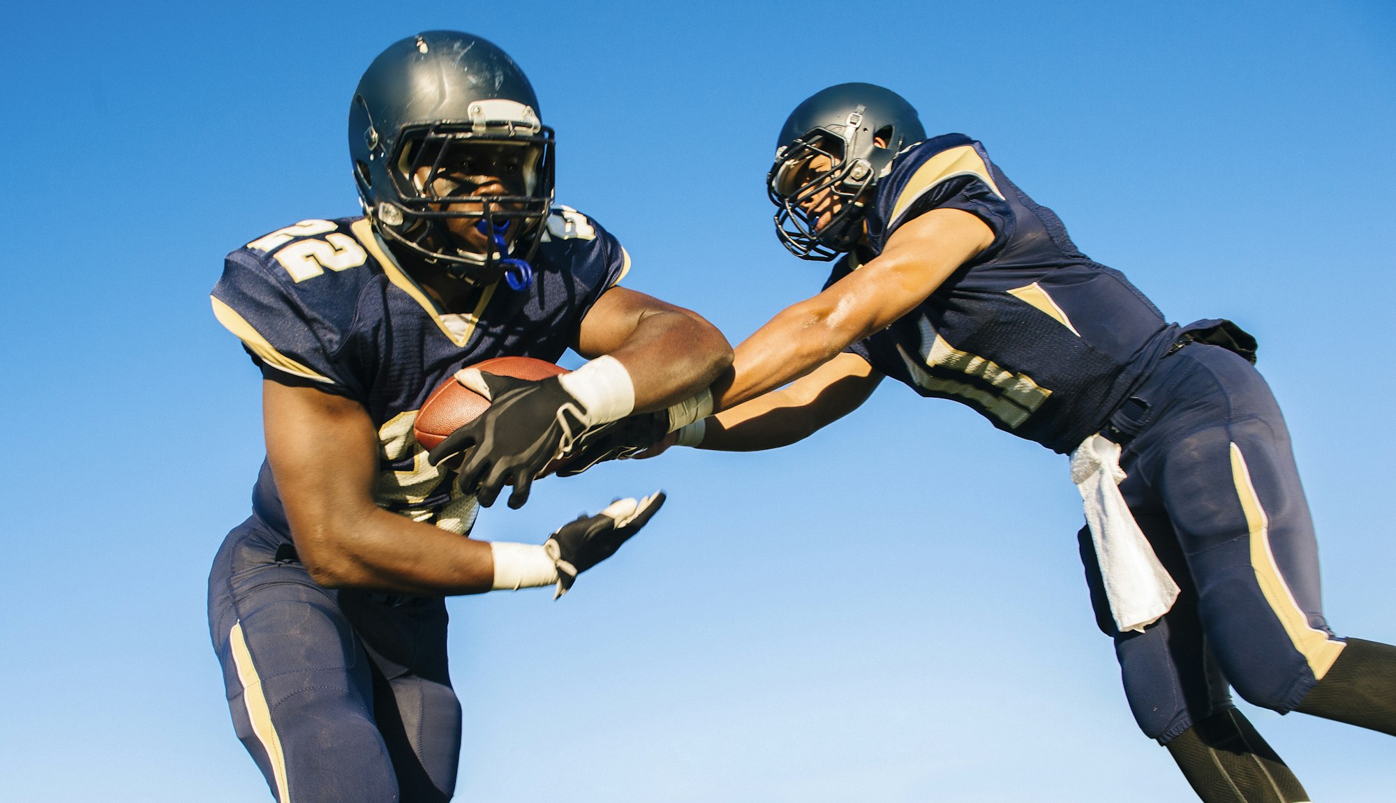Two teenage american football players tackling ball